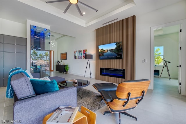 tiled living room with a large fireplace, ceiling fan, and a tray ceiling