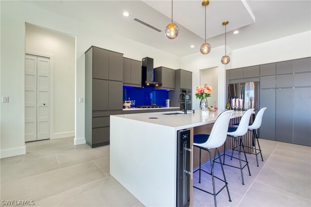 kitchen featuring wall chimney range hood, a kitchen breakfast bar, a kitchen island with sink, pendant lighting, and sink