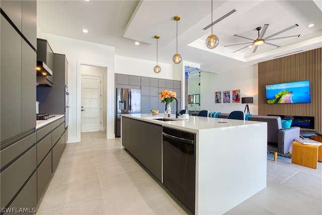 kitchen featuring an island with sink, pendant lighting, sink, ceiling fan, and a raised ceiling