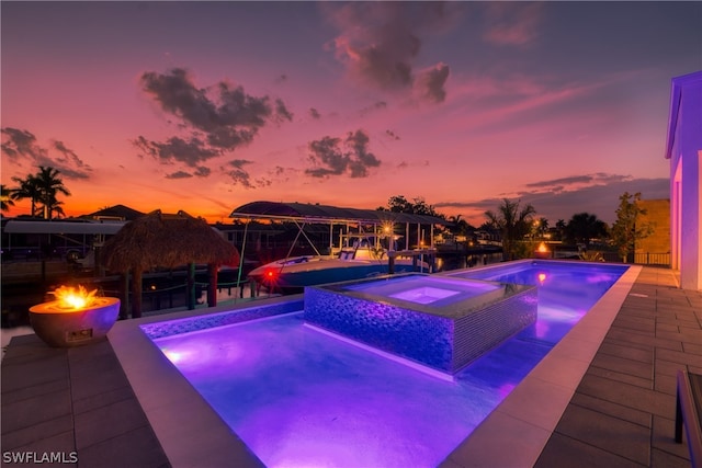 pool at dusk featuring a patio and an in ground hot tub