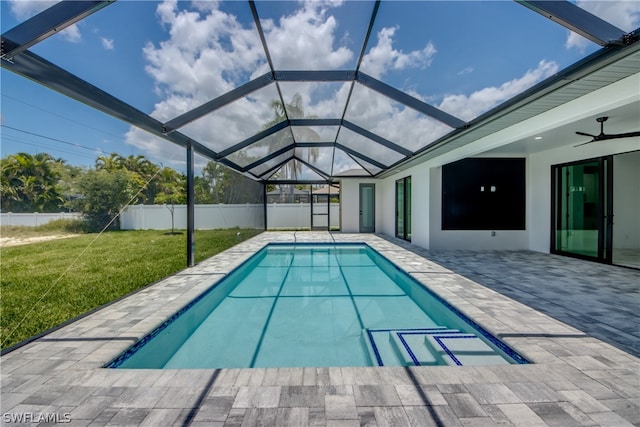 view of swimming pool featuring ceiling fan, a patio area, a lawn, and glass enclosure