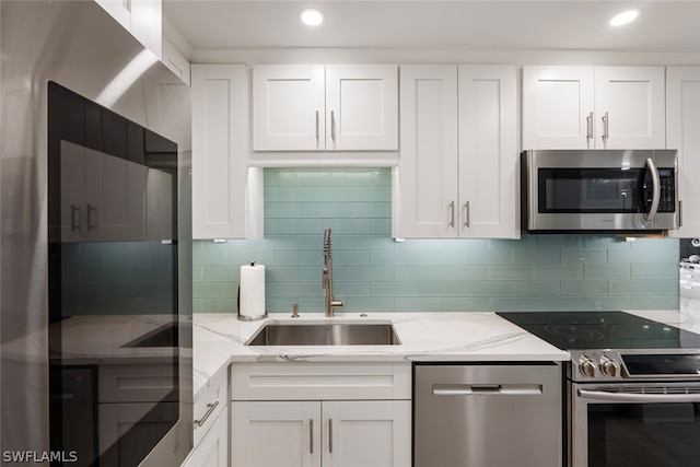 kitchen featuring sink, white cabinetry, appliances with stainless steel finishes, light stone countertops, and decorative backsplash