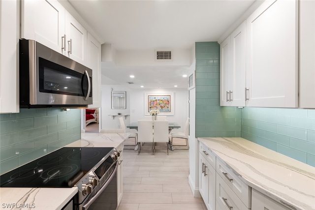 kitchen with stainless steel appliances, light stone countertops, decorative backsplash, and white cabinets