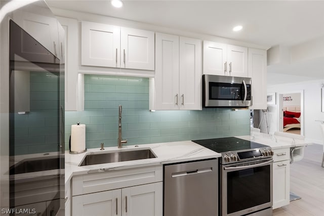 kitchen with sink, appliances with stainless steel finishes, white cabinetry, backsplash, and light stone counters