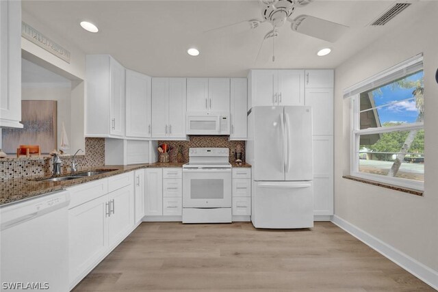 kitchen with white appliances, white cabinetry, a sink, and dark stone countertops