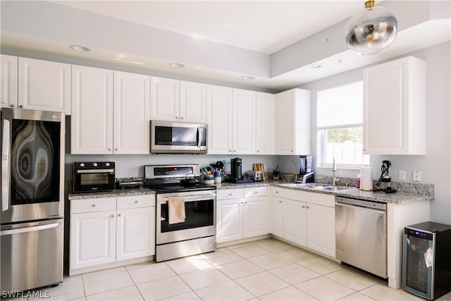 kitchen with appliances with stainless steel finishes, white cabinets, light stone counters, beverage cooler, and light tile floors