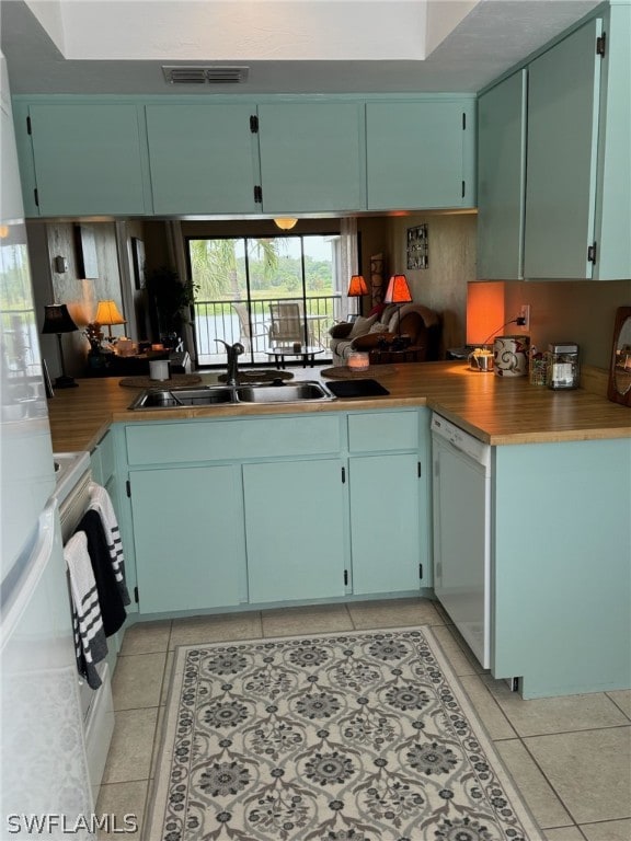 kitchen with sink, blue cabinets, white appliances, and light tile floors