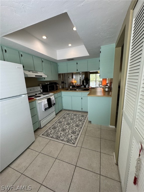 kitchen with white appliances, sink, light tile floors, and a raised ceiling