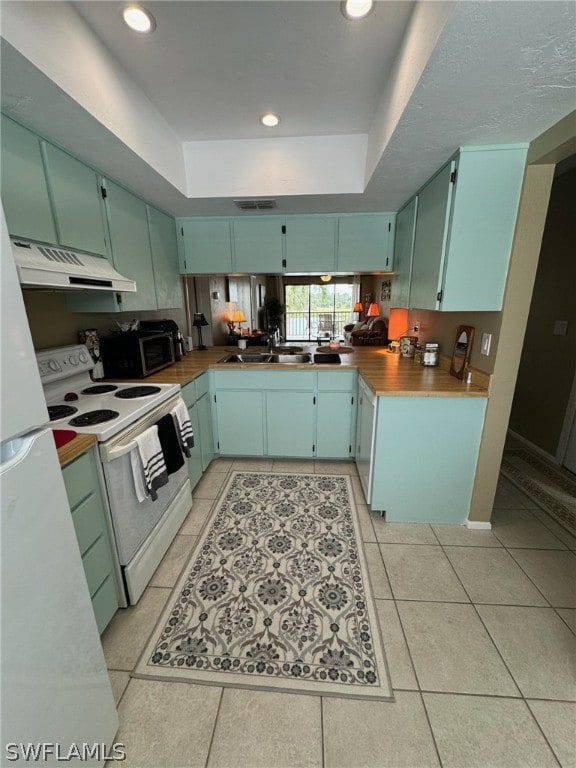 kitchen with blue cabinetry, white electric stove, light tile flooring, and a raised ceiling