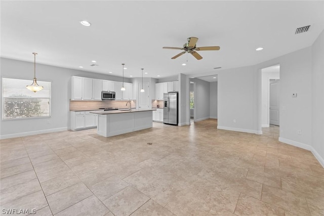 kitchen with appliances with stainless steel finishes, decorative backsplash, white cabinets, a center island with sink, and decorative light fixtures