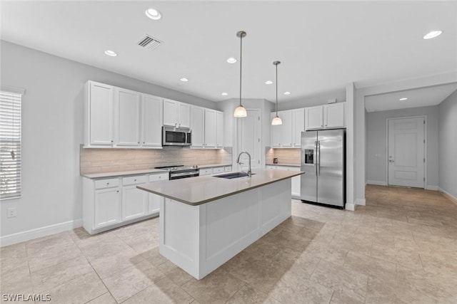 kitchen with appliances with stainless steel finishes, decorative light fixtures, sink, white cabinets, and a kitchen island with sink