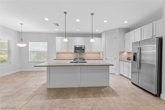 kitchen featuring stainless steel appliances, white cabinetry, hanging light fixtures, and a kitchen island with sink