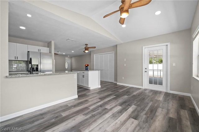 kitchen with dark wood finished floors, decorative backsplash, vaulted ceiling, a peninsula, and stainless steel fridge with ice dispenser