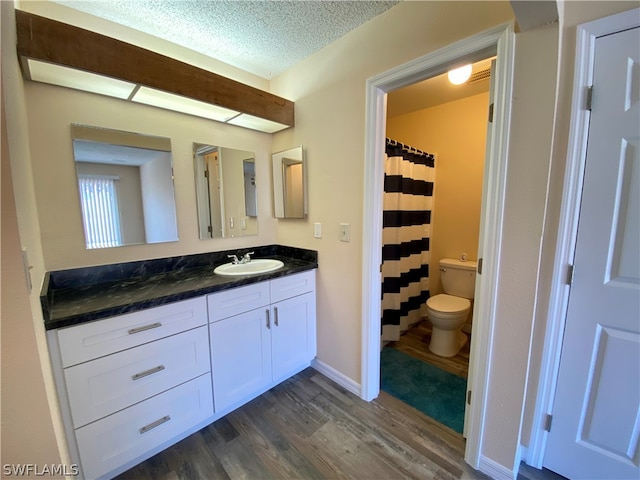 bathroom with vanity with extensive cabinet space, toilet, hardwood / wood-style flooring, and a textured ceiling