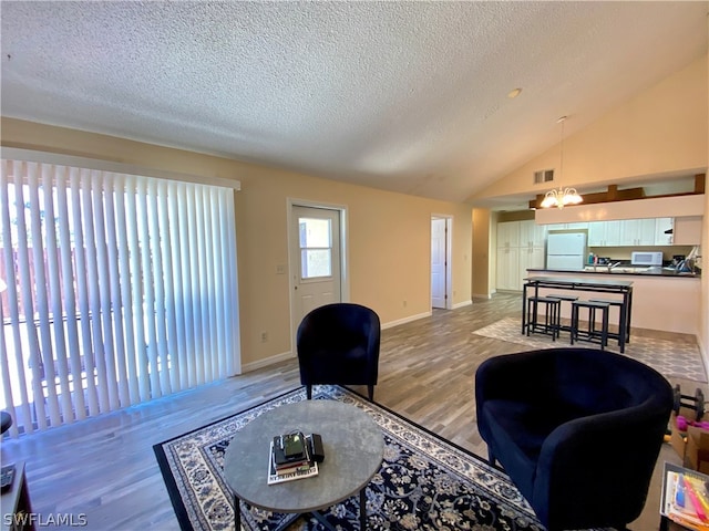 living room with high vaulted ceiling, light hardwood / wood-style flooring, a textured ceiling, and an inviting chandelier