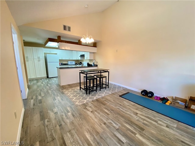 kitchen with hanging light fixtures, white cabinets, kitchen peninsula, wood-type flooring, and white fridge