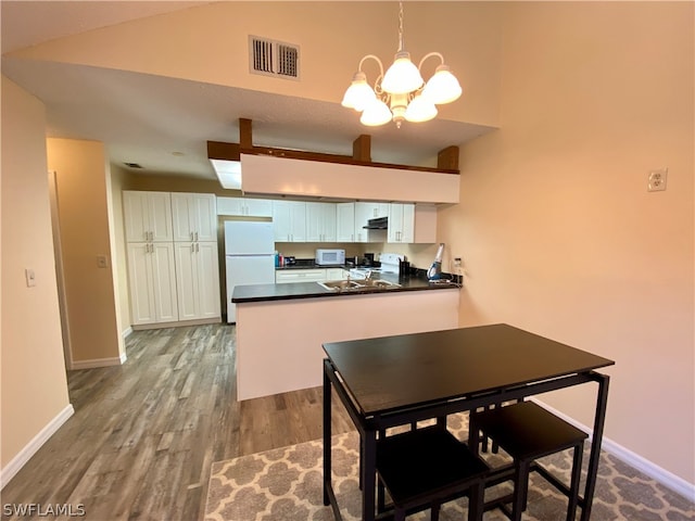 kitchen with kitchen peninsula, white appliances, an inviting chandelier, hardwood / wood-style flooring, and white cabinetry