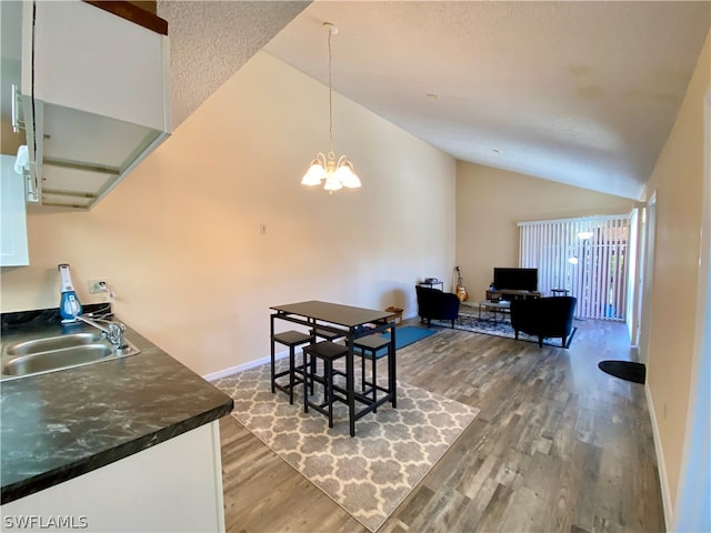 dining area featuring sink, hardwood / wood-style flooring, high vaulted ceiling, and an inviting chandelier