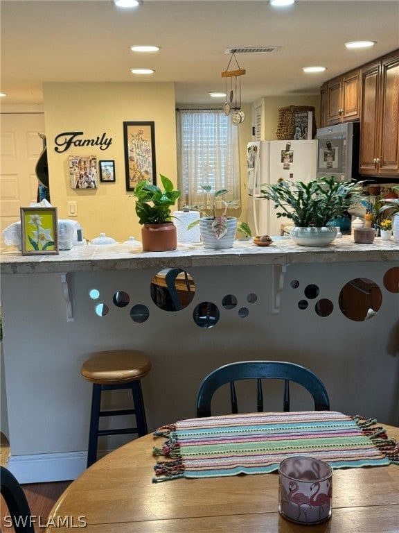 kitchen with a kitchen breakfast bar, decorative light fixtures, white fridge, and wood-type flooring