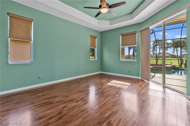 empty room with hardwood / wood-style floors, ceiling fan, and a raised ceiling