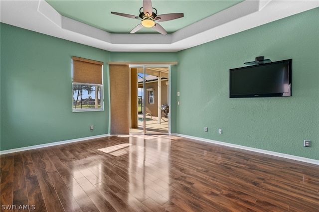 unfurnished room featuring a raised ceiling, ceiling fan, and hardwood / wood-style flooring