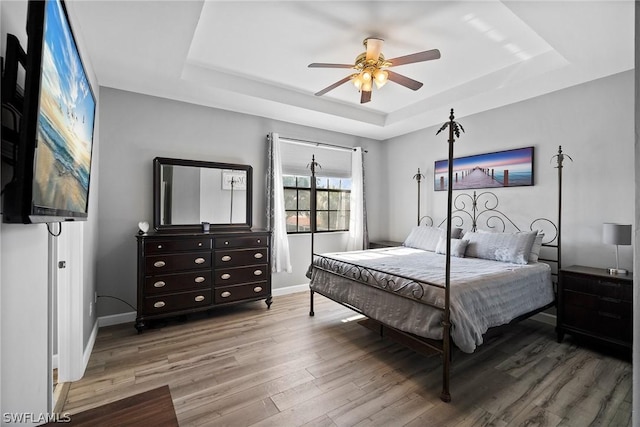 bedroom with wood-type flooring, a raised ceiling, and ceiling fan