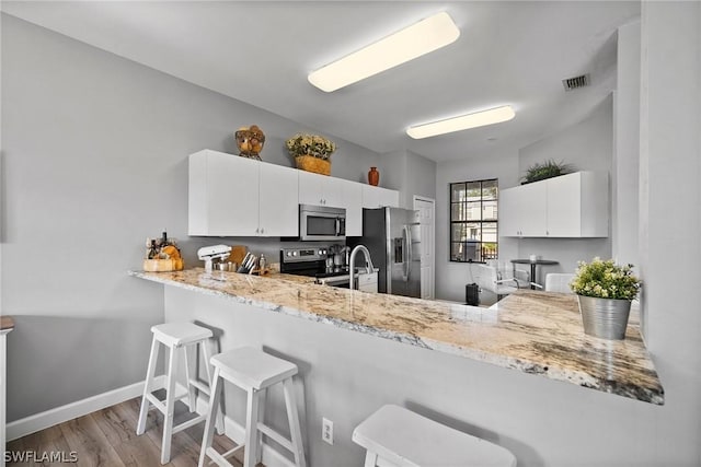 kitchen featuring a kitchen breakfast bar, kitchen peninsula, white cabinets, and appliances with stainless steel finishes