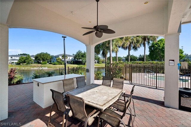 view of patio featuring ceiling fan, a water view, and a fenced in pool