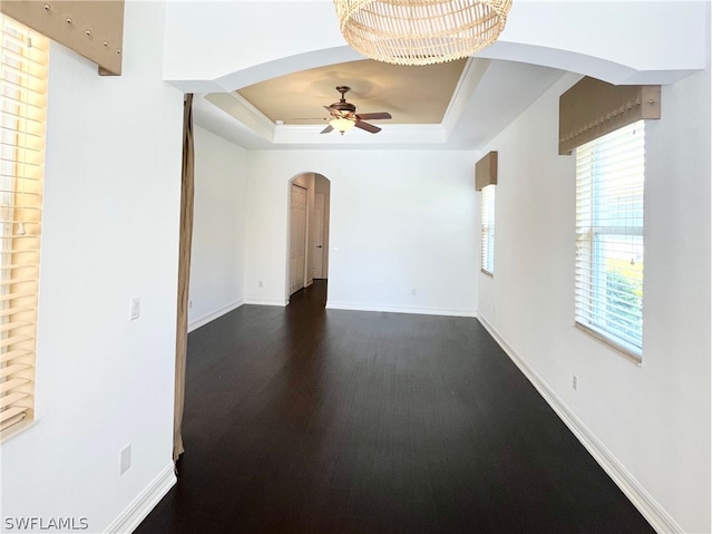 spare room with ceiling fan with notable chandelier, dark hardwood / wood-style flooring, and a raised ceiling