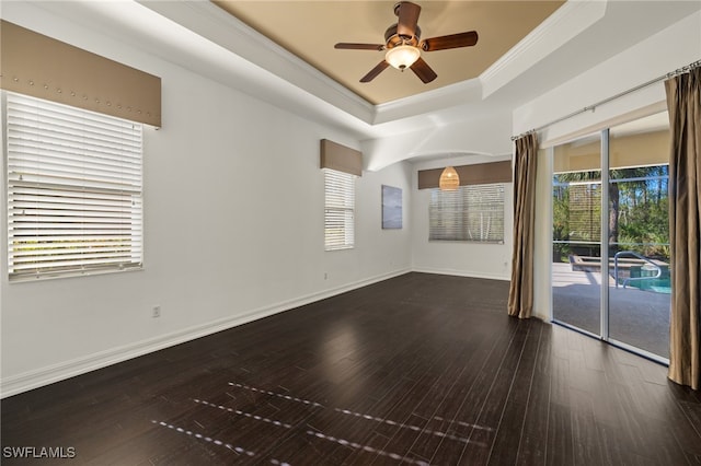 unfurnished room with ceiling fan, crown molding, dark wood-type flooring, and a tray ceiling