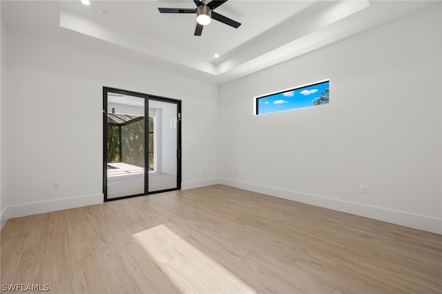 spare room with a tray ceiling, ceiling fan, and light hardwood / wood-style floors