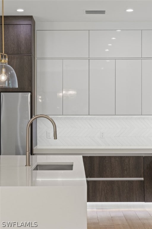 kitchen featuring pendant lighting, dark brown cabinets, stainless steel fridge, and white cabinetry