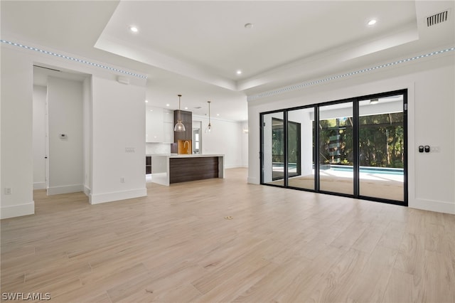 unfurnished living room with light wood-type flooring, a raised ceiling, and sink