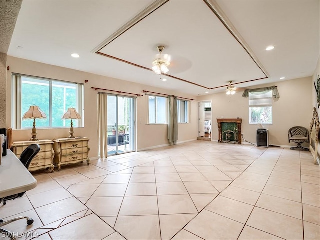 tiled living room with ceiling fan and a tray ceiling