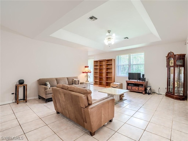 living room featuring a raised ceiling, ceiling fan, and light tile patterned floors