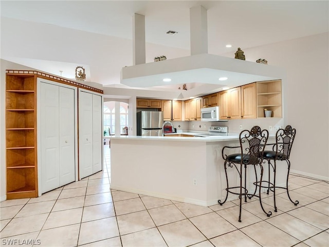 kitchen featuring light tile patterned floors, electric range oven, kitchen peninsula, a breakfast bar area, and stainless steel refrigerator