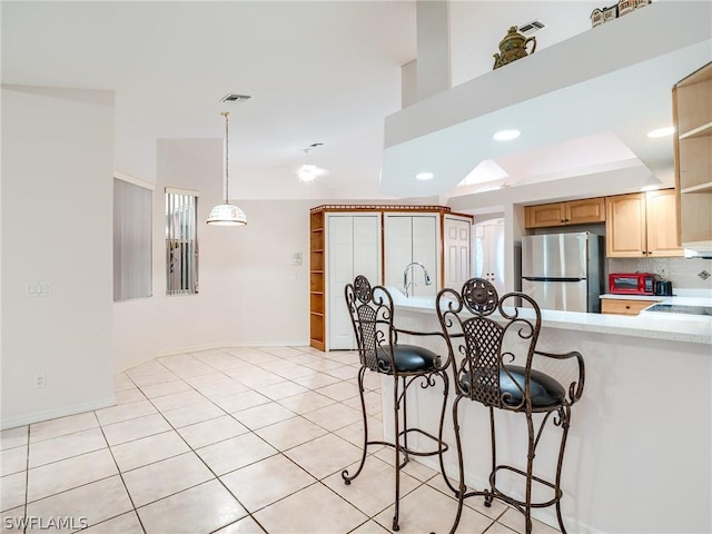 kitchen featuring stainless steel fridge, light tile patterned floors, hanging light fixtures, and light brown cabinets