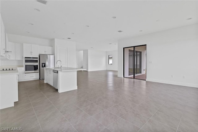 kitchen with sink, light tile patterned floors, an island with sink, stainless steel appliances, and white cabinets