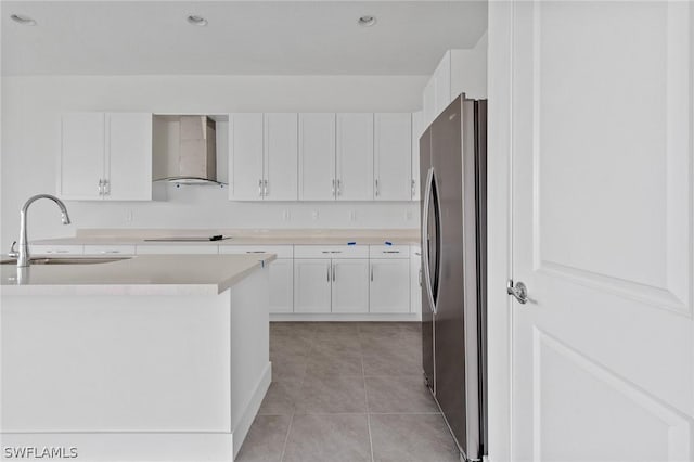 kitchen with sink, stainless steel fridge, white cabinetry, black electric cooktop, and wall chimney exhaust hood