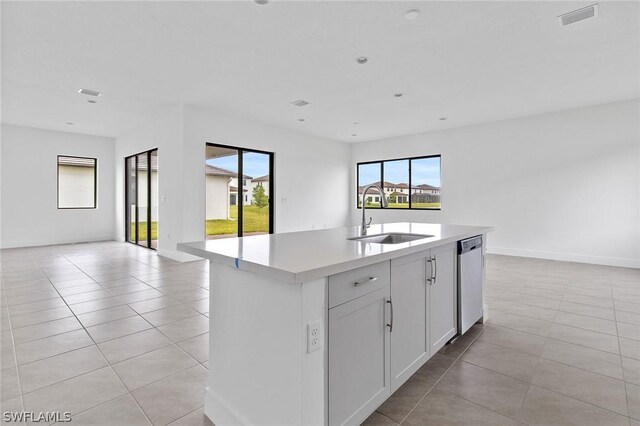 kitchen with sink, light tile patterned floors, stainless steel dishwasher, an island with sink, and white cabinets