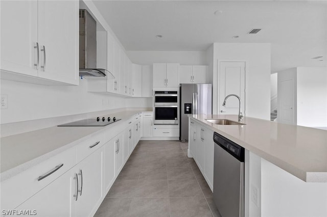 kitchen with appliances with stainless steel finishes, sink, white cabinets, light tile patterned floors, and wall chimney range hood