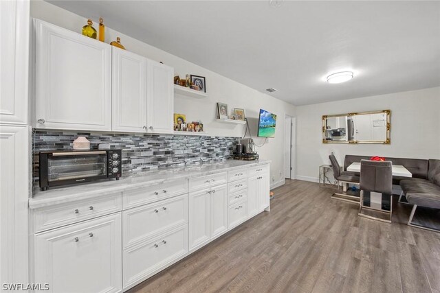 kitchen with light stone countertops, hardwood / wood-style floors, tasteful backsplash, and white cabinetry