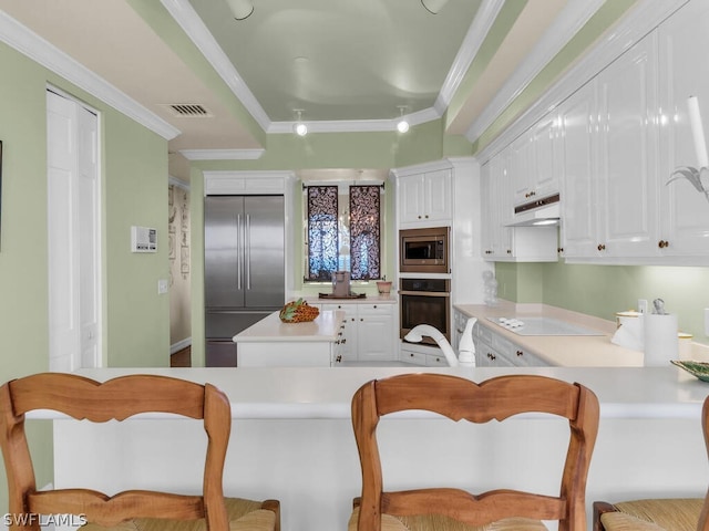 kitchen with a kitchen breakfast bar, built in appliances, white cabinetry, and crown molding