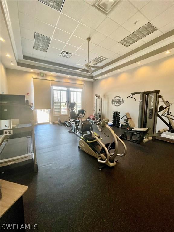 workout area with a paneled ceiling, a tray ceiling, and ceiling fan