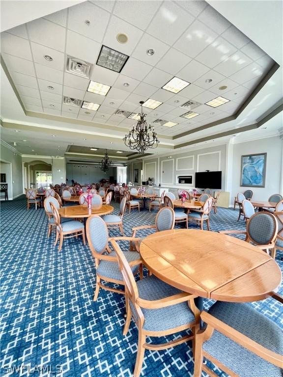 carpeted dining area with a raised ceiling, a drop ceiling, and an inviting chandelier