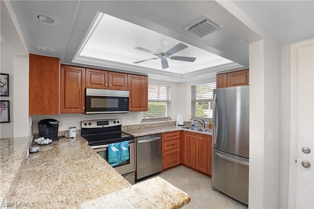 kitchen featuring ceiling fan, sink, light stone counters, a tray ceiling, and appliances with stainless steel finishes