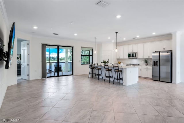 kitchen featuring appliances with stainless steel finishes, a breakfast bar, a center island with sink, white cabinetry, and hanging light fixtures