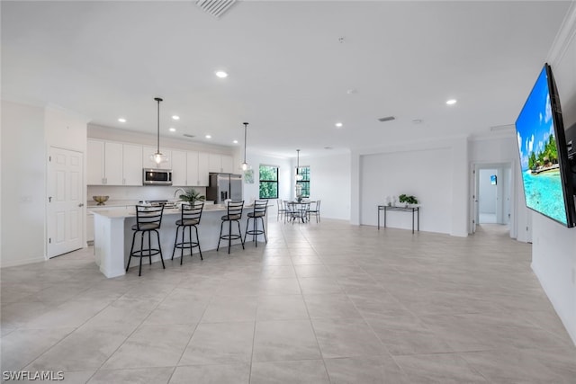 kitchen with appliances with stainless steel finishes, pendant lighting, a center island with sink, white cabinets, and ornamental molding