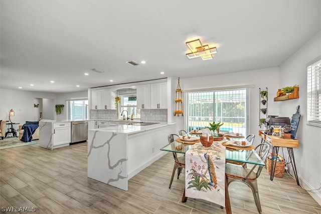 kitchen featuring kitchen peninsula, sink, dishwasher, light hardwood / wood-style floors, and white cabinetry