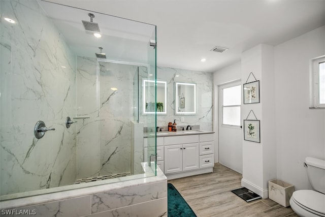 bathroom with hardwood / wood-style floors, vanity, a tile shower, and plenty of natural light